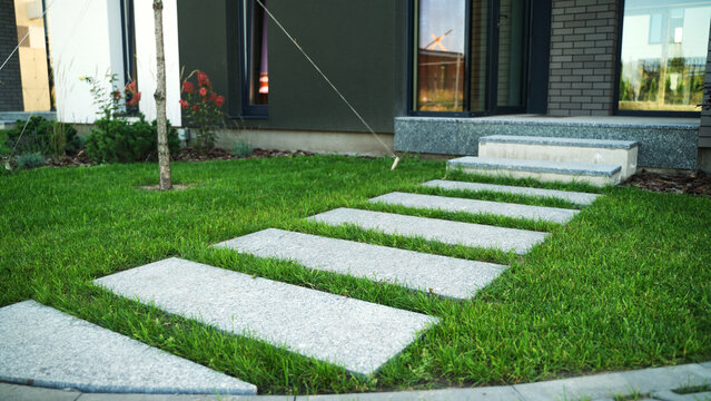 Modern house garden featuring stone stepping path on green lawn leading to entrance stairs