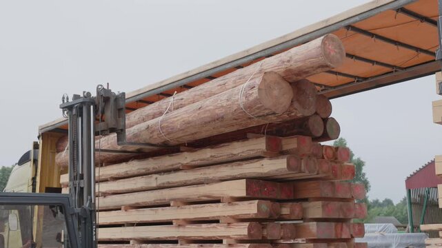 Forklift lifting stacked logs and rough-sawn timber beside a transport truck at an outdoor lumber yard, showing wood handling and industrial logistics