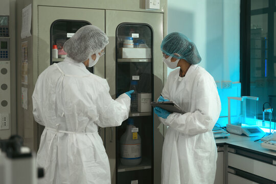 Two Pharmaceutical Lab Technicians in Protective Gear Conducting Quality Control Inventory Check in Research Laboratory