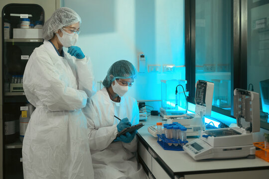 Pharmaceutical Lab Scientists in Protective Gear Conducting Quality Control Research with Laboratory Equipment