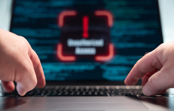 Finger typting on the laptop keyboard, blurred warning sign unauthorized access on the screen, computer crime. Hacker, data, code, encryption, data breach, spyware, security, firewall.