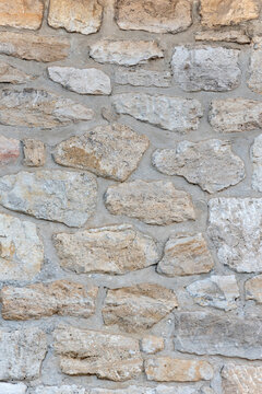 Close up showing a rustic stone wall with irregular, light colored blocks and rough texture, creating a traditional background pattern for various design needs