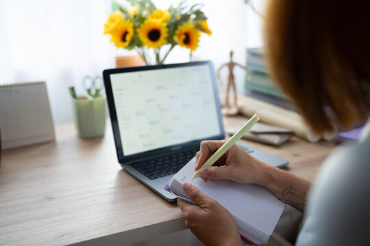 A white woman writes notes while working remotely at home in Spain