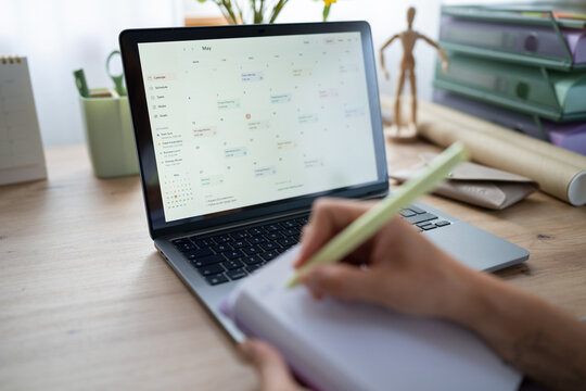 White Person planning schedule using a laptop calendar and notebook