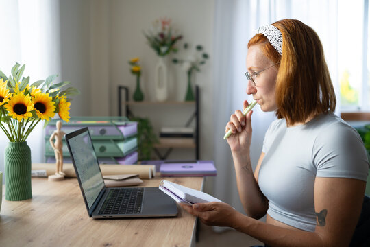 A white woman works thoughtfully in a bright home office in a office