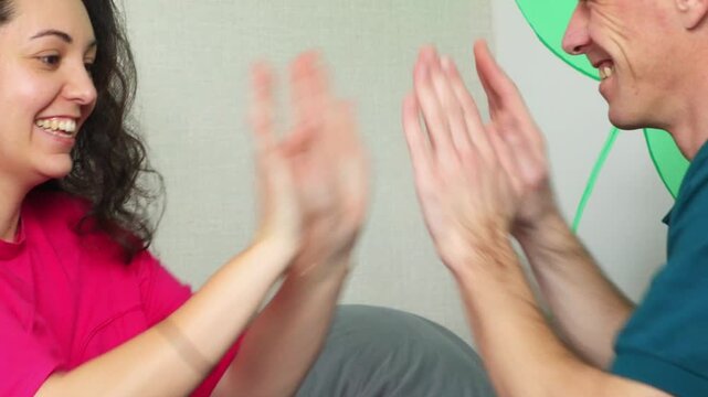 Young couple enjoying a fun shared activity while sitting together on a bed. Their hand clapping game, smiles, and conversation demonstrate intimacy, companionship, communication. Close up.