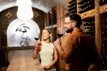 Naklejka premium Couple enjoys wine tasting in a cellar at a vineyard during an evening visit