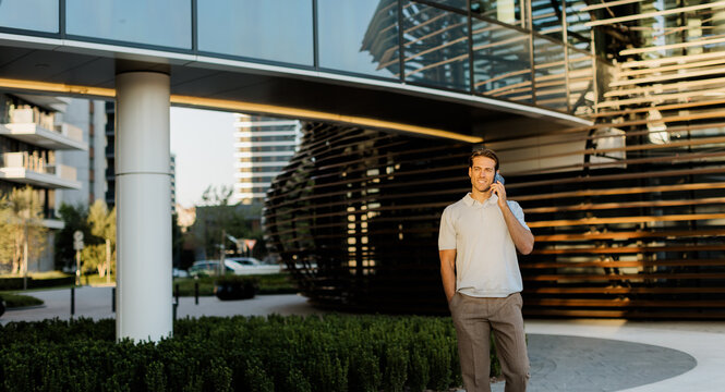 Man talking on phone near modern building in bright evening light