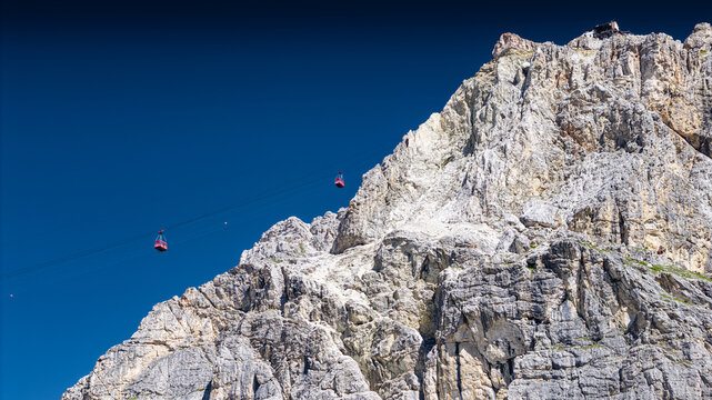 Aerial view of red cable cars traversing the rugged rocky slopes of Falzarego Pass in the Dolomites, Cortina d'Ampezzo, Veneto, Italy.