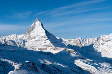 Obraz premium Iconic Matterhorn peak rising above pristine snow-covered Alpine slopes under a clear blue winter sky.