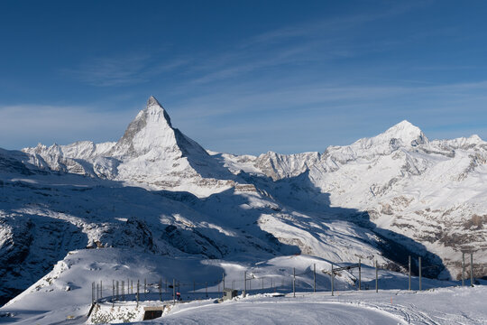 Snow-covered Matterhorn rises above alpine ski slopes near Zermatt beneath a clear blue winter sky.