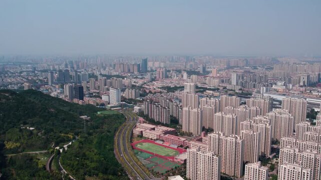 This aerial image shows a dense urban residential district adjacent to a green mountain, with a sports field and road running through the area, forming a city landscape.