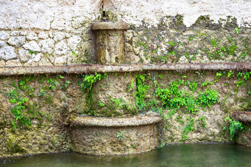 Fototapeta premium Old stone fountain against weathered wall in rustic courtyard