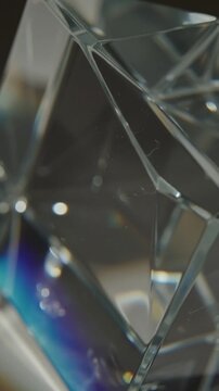 Macro close-up of a transparent crystal glass prism dispersing white light into rainbow spectrum colors with bokeh on a dark dramatic background
