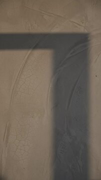 Close-up of cracked beige plaster or aged ceramic surface with fine crazing patterns and a moving shadow line creating a minimal architectural texture