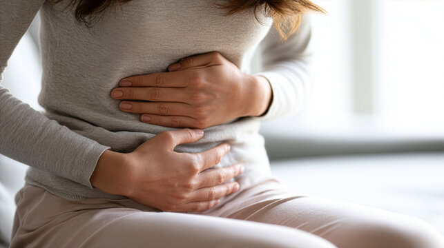 A  young woman's hands gently supporting her lower abdomen while seated comfortably women's health, menstrual pain, digestive wellness, clean medical advertising concept