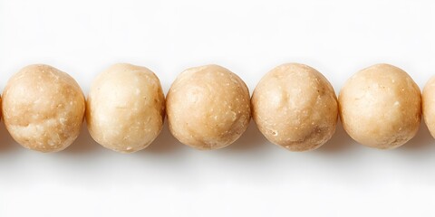 Fototapeta premium Several round macadamia nuts are arranged in a horizontal line against a white background.