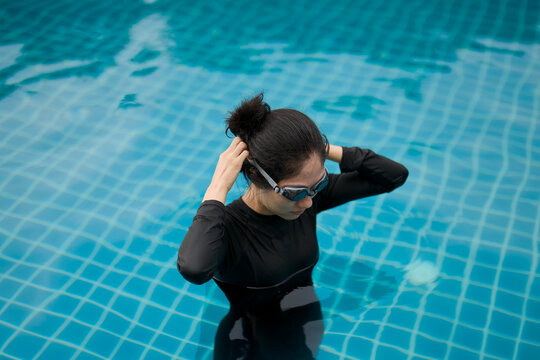 Asian woman wearing swimming goggles tying her hair in a pool