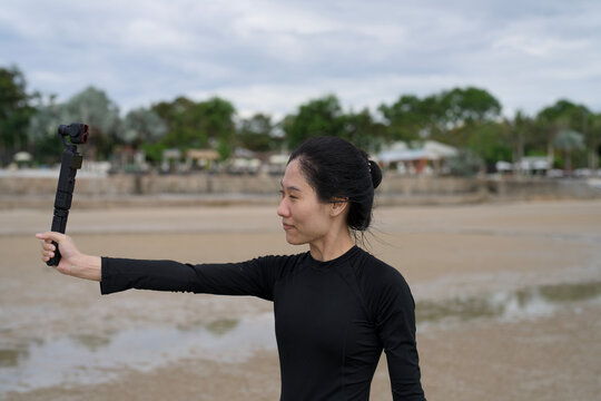 Woman holding a gimbal camera filming a vlog on a tropical beach