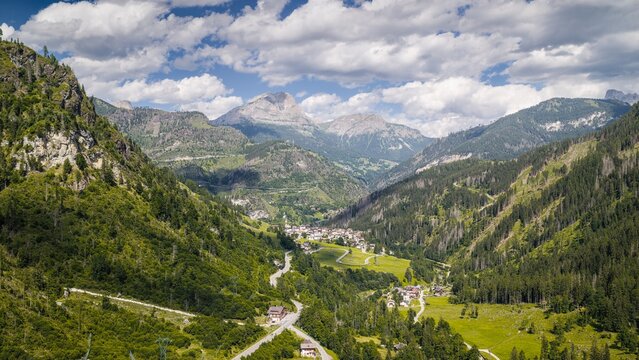 Aerial view of Col di Rocca village nestled in a lush green valley surrounded by the towering peaks of the Dolomites, with pine forests and winding roads in Col di Rocca, Veneto, Italy.