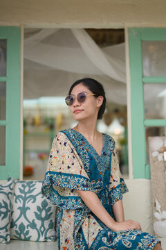 Asian woman in a batik kaftan and sunglasses relaxing at a beach cafe