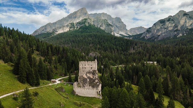 Aerial view of Castello di Andraz, a historic stone fortress nestled in pine forests of the Dolomites, surrounded by mountain peaks in Livinallongo del Col di Lana, Veneto, Italy.