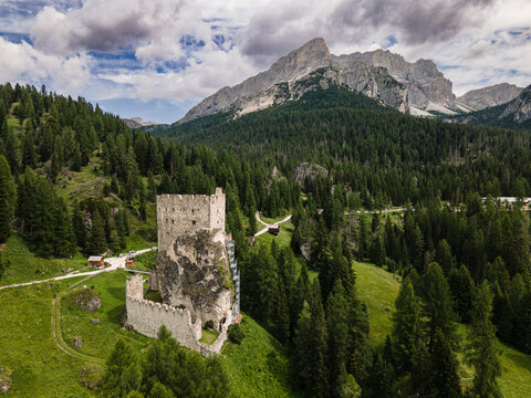 Aerial view of Castello di Andraz surrounded by dense pine forests and dramatic mountain peaks under a cloudy sky in Livinallongo del Col di Lana, Veneto, Italy.