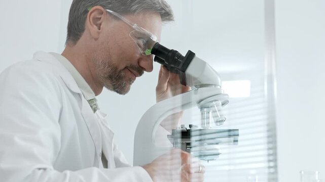 Male scientist focused on his research, looking through a microscope in a bright laboratory, making advancements in medicine and biology