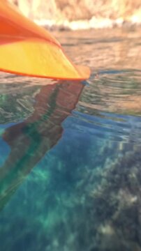 Kayak paddle water glides through clear turquoise sea revealing rocky seabed and sunlight reflections during a peaceful summer adventure