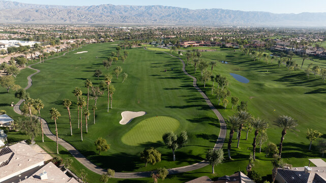 Aerial view of a lush green golf course with palm trees, sand bunkers, and winding paths in a residential area in Indio, California, United States.