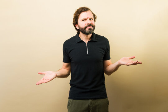 Confused man shrugging shoulders, making a gesture of uncertainty or not knowing against a plain background