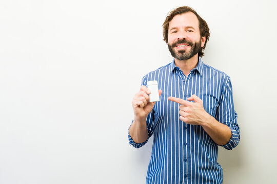 Smiling man presenting a white bottle, pointing at it, recommending supplements or medication for health and wellness