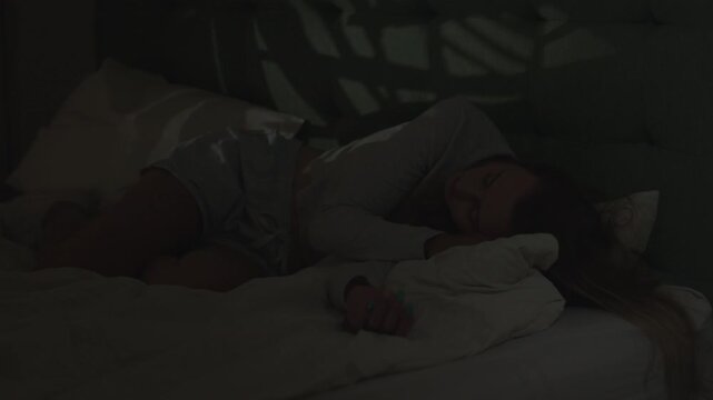 Woman in a dark bedroom. Lying in bed exhausted and unable to sleep. Suffering from depression and anxiety