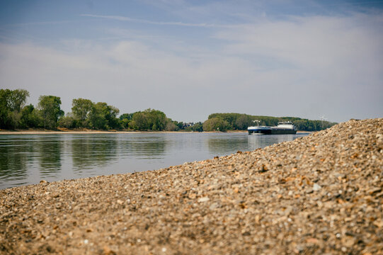 Extremes Niedrigwasser am Rhein mit freiliegendem Kiesufer und Frachtschiffen auf dem Fluss als Symbol f&uuml;r D&uuml;rre, Wasserknappheit und Probleme der Binnenschifffahrt.
