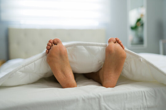 Woman's feet relaxing on a bed, covered by a white duvet. Concepts of comfort, sleep, and a peaceful morning