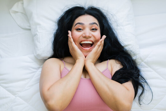 Young woman feeling surprised and happy, looking excited with open mouth in bed after waking up