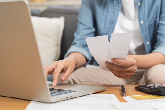 Close up of a person hand holding receipts while using laptop and calculator for home budget planning, financial management, monthly expense tracking and tax calculation