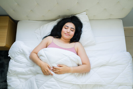 High angle view of a woman enjoying deep sleep in a comfortable bed, finding rest and relaxation in her peaceful bedroom