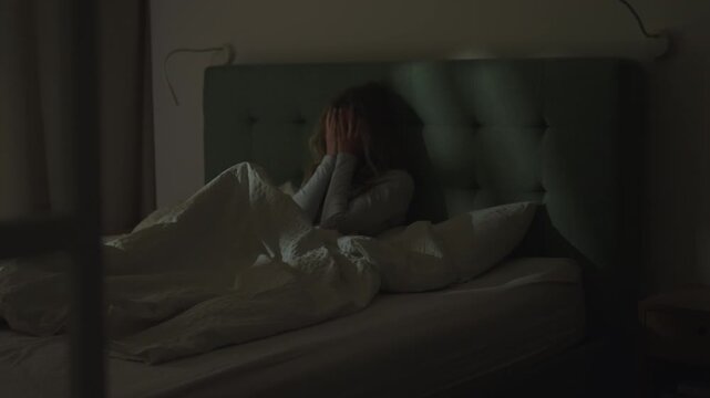 Woman in a dark bedroom. Lying in bed exhausted with face in hands unable to sleep. Suffering from depression and anxiety