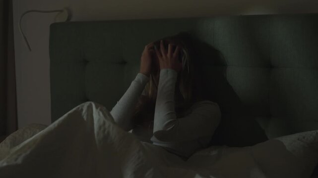 Woman in a dark bedroom. Lying in bed exhausted with face in hands unable to sleep. Suffering from depression