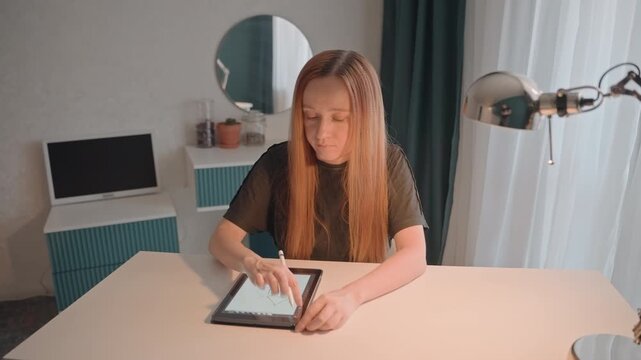 Young woman with long straight hair draws geometric shapes. Tablet shows evolving geometric forms as pen moves. Room features light desk where young woman sits surrounded