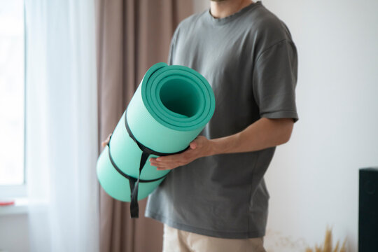 Someone holds a green yoga mat while entering a room with sunlight coming through the window
