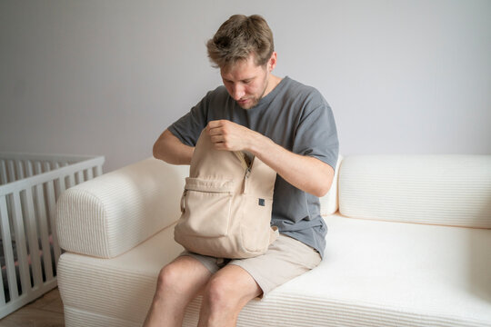 A man checks the contents of his backpack while sitting on a couch in a home setting