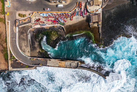 Aerial view of colorful fishing boats at the harbor in Ponta do Sol, with turquoise waves crashing against the rocky coastline of Santo Antao, Ponta do Sol, Ribeira Grande, Cabo Verde.