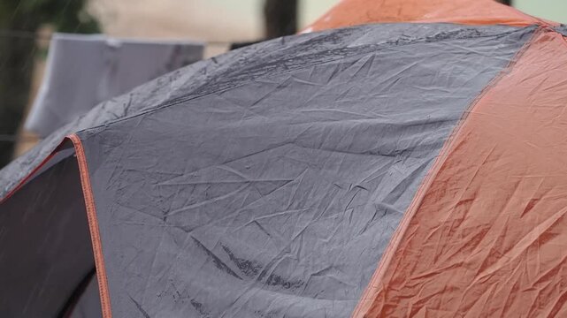 Durable grey and orange waterproof tent on a wooden deck during the rain.