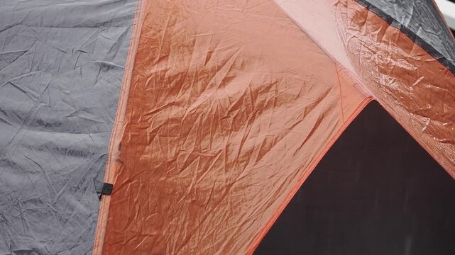 Durable grey and orange waterproof tent on a wooden deck during the rain.