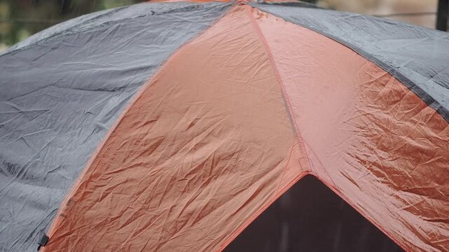 Durable grey and orange waterproof tent on a wooden deck during the rain.