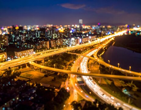Aerial night view of a sprawling cityscape, complex highways, and illuminated buildings
