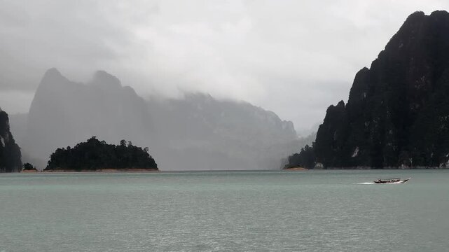 Ratchaprapha Dam on a rainy day at khao sok national park, surat thani province thailand featuring spectacular limestone mountains shrouded in mist.