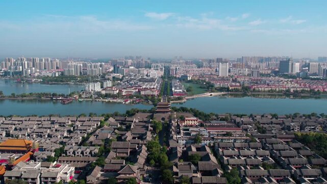 Aerial shot shows an ancient city with moat and traditional buildings, adjacent to modern urban areas under clear blue sky.